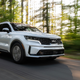 A photo of a white Kia Sorento SUV driving along a tree-lined road.